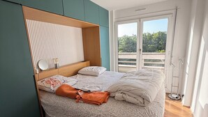 Ein Schlafzimmer mit einem Bett, einem Nachttisch, einem Spiegel und Blick ins Freie.