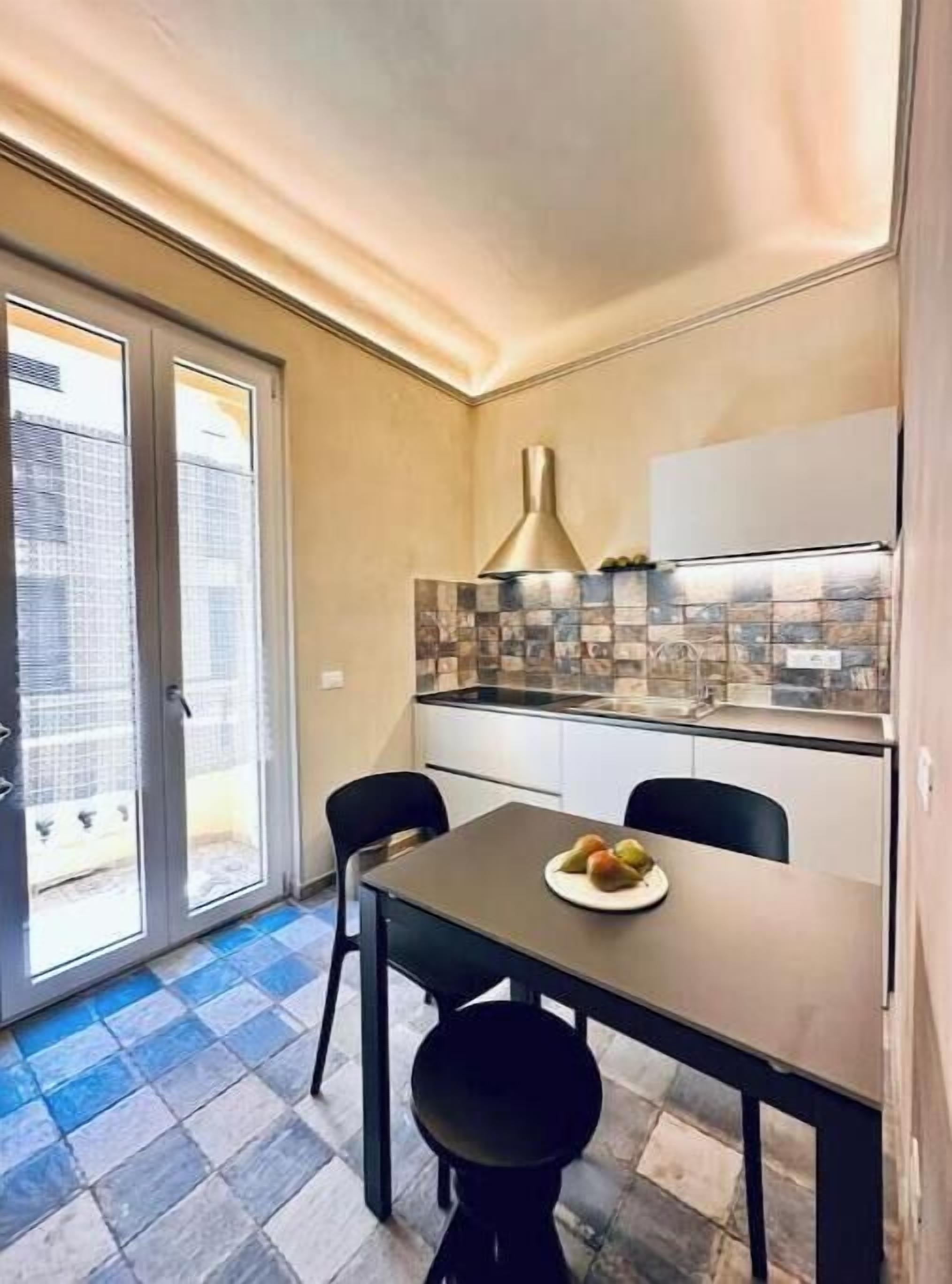 A compact kitchen with a tiled backsplash, a modern stove, and a dining area with two chairs and a table.