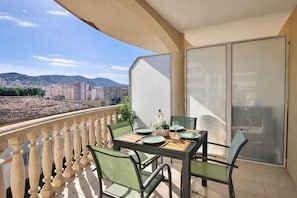 Un balcon avec une table dressée pour deux personnes, des chaises et une vue sur le paysage urbain.