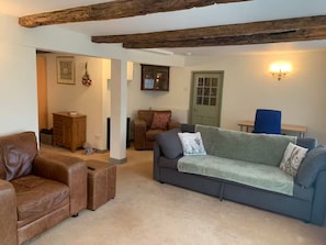 Ein gemütliches Wohnzimmer mit einem braunen Ledersofa, einem grauen Sofa mit Decke, einem Holzkabinett und einem blauen Sessel.