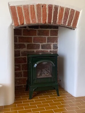 Ein Eckzimmer mit Kamin aus Backsteinen, einem grünen Herd und einem Fliesenboden.