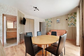 Una habitación con una mesa redonda de madera, sillas negras, un televisor montado en la pared y un papel tapiz estampado en una pared.