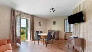 Ein Zimmer mit Esstisch, Stühlen, einer Couch, einem Fernseher und einem Kamin.