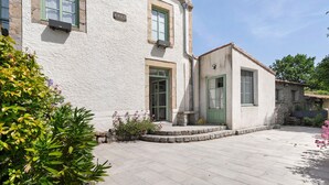Ein zweistöckiges Gebäude mit einer Stein-Fassade, ein kleiner Anbau mit einer grünen Tür und ein gepflasterter Innenhof.