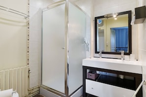 Un baño con cabina de ducha de vidrio, un lavamanos blanco con encimera oscura y un espejo sobre el lavamanos.