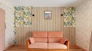 Ein Zimmer mit Holzboden, einem rosafarbenen Sofa und einer Wand mit tropischem Blattmuster.