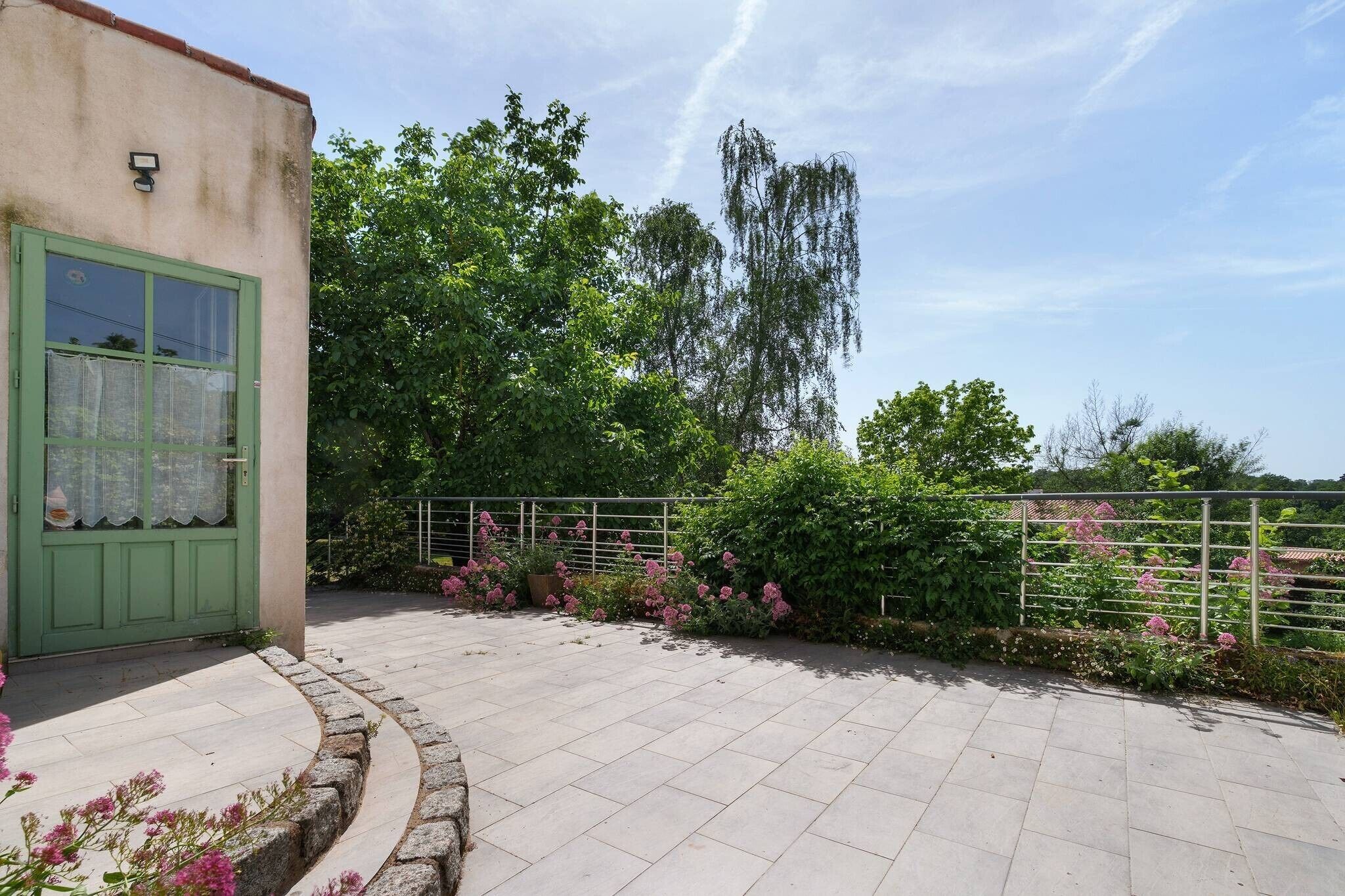 Un bâtiment avec une porte verte, une cour pavée et une clôture en métal.