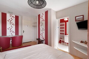 A bedroom with a bed, a desk, a chair, a TV, and a door leading to another room.