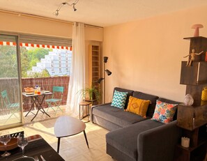 Ein Wohnzimmer mit einer Couch, einem Esstisch mit Stühlen, einer Zimmerpflanze und Blick durch eine Glastür.