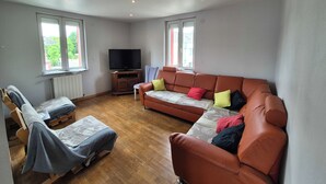 Ein Wohnzimmer mit einer Couch, einem Liegesessel, einem Fernseher und einem Fenster.