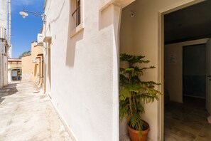 Un stretto vicolo con un edificio bianco, una pianta in vaso e una porta che dà su una stanza.