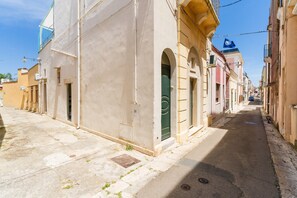 Un vicolo stretto fiancheggiato da edifici, alcuni con porte e finestre visibili, e un cielo azzurro sopra.