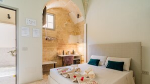 A hotel room with a large bed, a stone wall, a small desk, and a bathroom. - Apartment 'Luxury Rooms - Elisa' with Wi-Fi and Air Conditioning (Alezio)