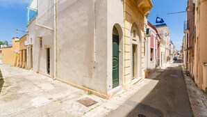 Eine enge Straße mit Gebäuden an beiden Seiten, einige mit sichtbaren Türen und Fenstern, und einem strahlend blauen Himmel darüber.