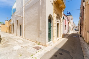 Eine enge Straße mit Gebäuden an beiden Seiten, einige mit sichtbaren Türen und Fenstern, und einem strahlend blauen Himmel darüber.