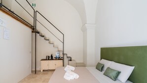 Ein Hotelzimmer mit Bett, einem grünen Kopfteil, einer Treppe, einem kleinen Schrank mit Toilettenartikeln und einem Schild, das einen Feuerausgang kennzeichnet.