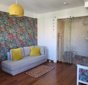 A living room with a sofa, a yellow pendant light, a patterned wall, a woven curtain, and a wooden floor. - Bright apartment in Toulon (Toulon)