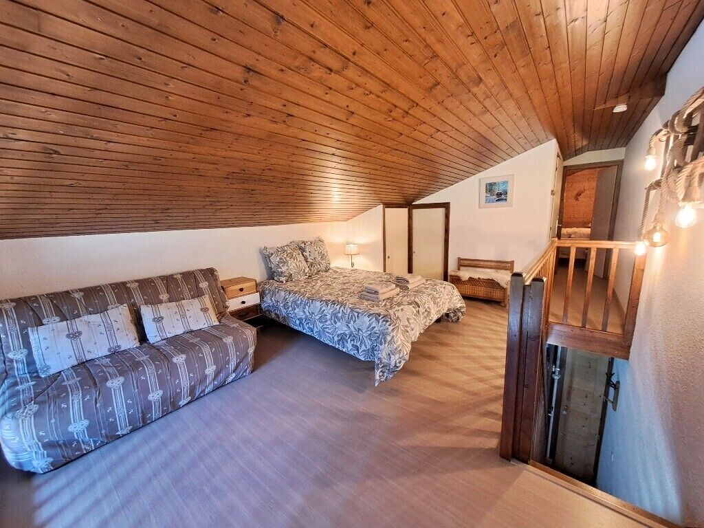 Een slaapkamer met een houten plafond, een bed, een bank en een trap.