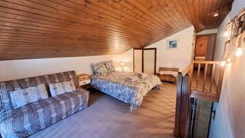 Een slaapkamer met een houten plafond, een bed, een bank en een trap.