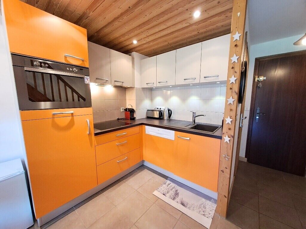 Een keuken met oranje kastjes, een roestvrijstalen oven, een spoelbak en een houten plafond.