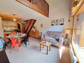 A spacious living area with a dining table, a sofa, and a staircase leading to an upper level. - Bright apartment in the village center (Le Grand-Bornand)