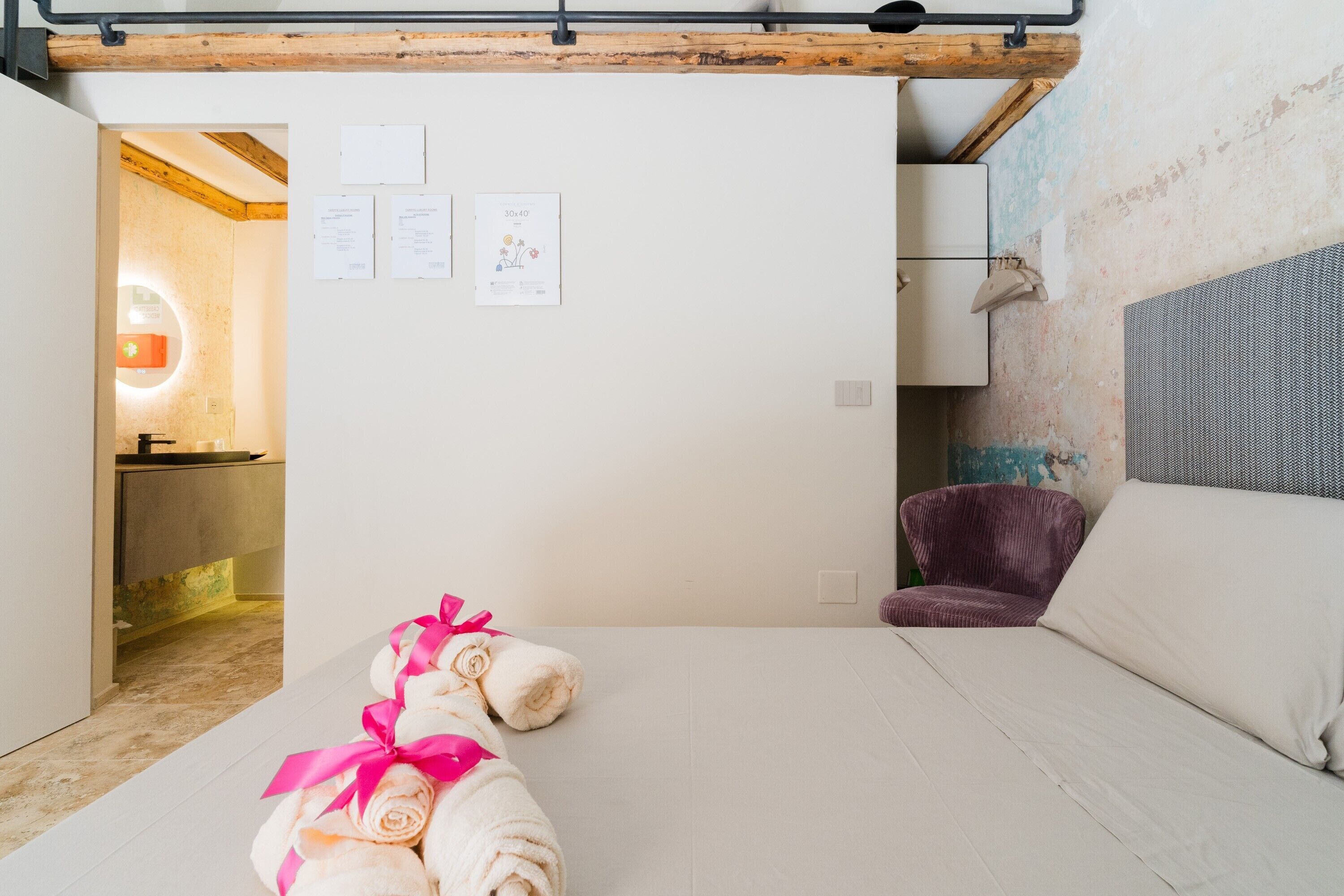Une chambre d’hôtel avec un lit, une chaise, un mur recouvert de papiers et une poutre en bois au plafond.