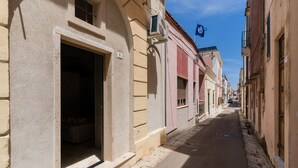 A narrow street with buildings on either side, a clear sky, and a flag hanging from one building. - Suite 'Luxury Rooms - Erika' with Wi-Fi and Air Conditioning (Alezio)