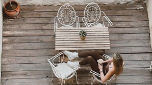 En træterrasse med et bord, stole og en potteplante. En person sidder der.
