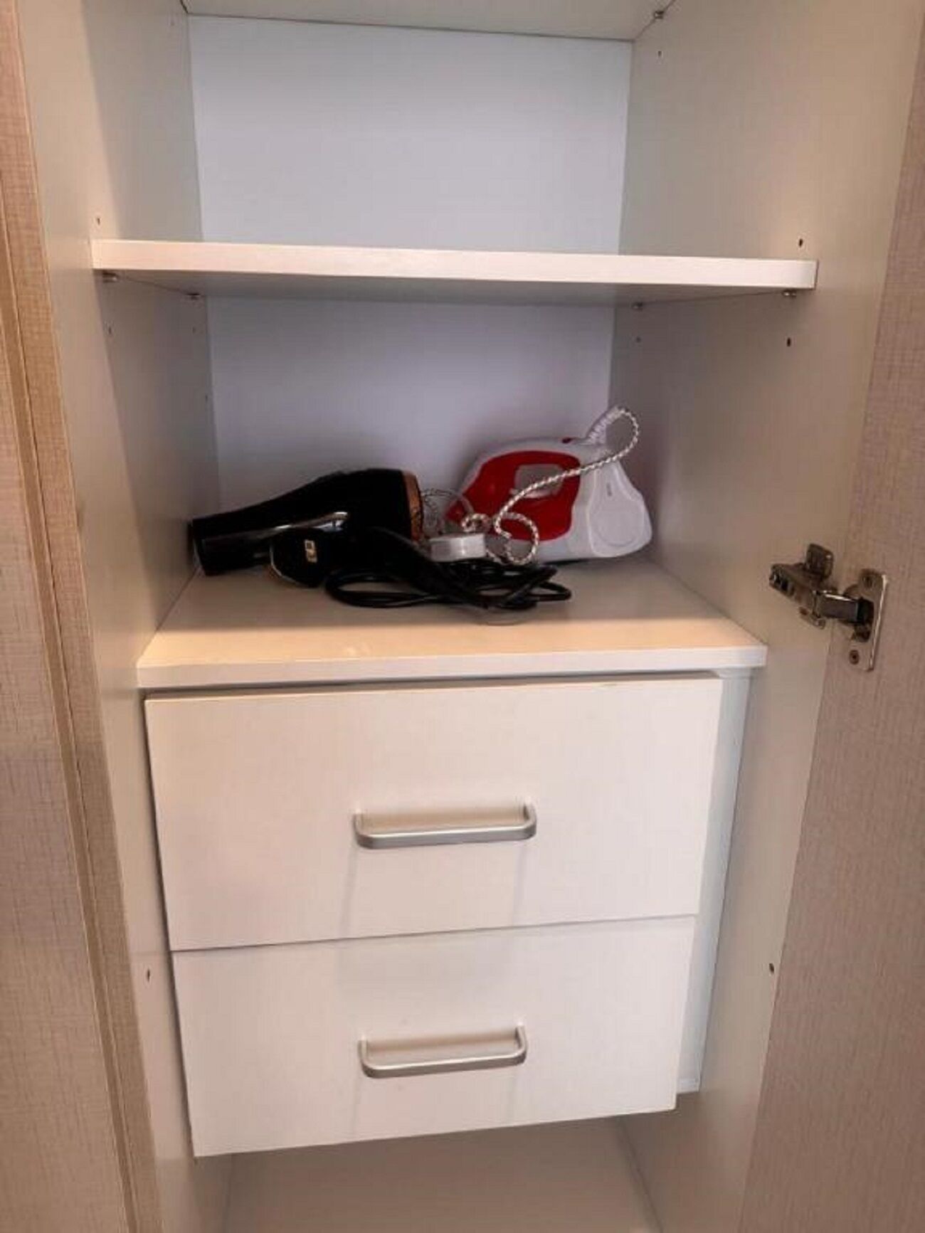 Un meuble blanc avec deux tiroirs et une étagère au-dessus, contenant un sac à main rouge et blanc et un objet noir.