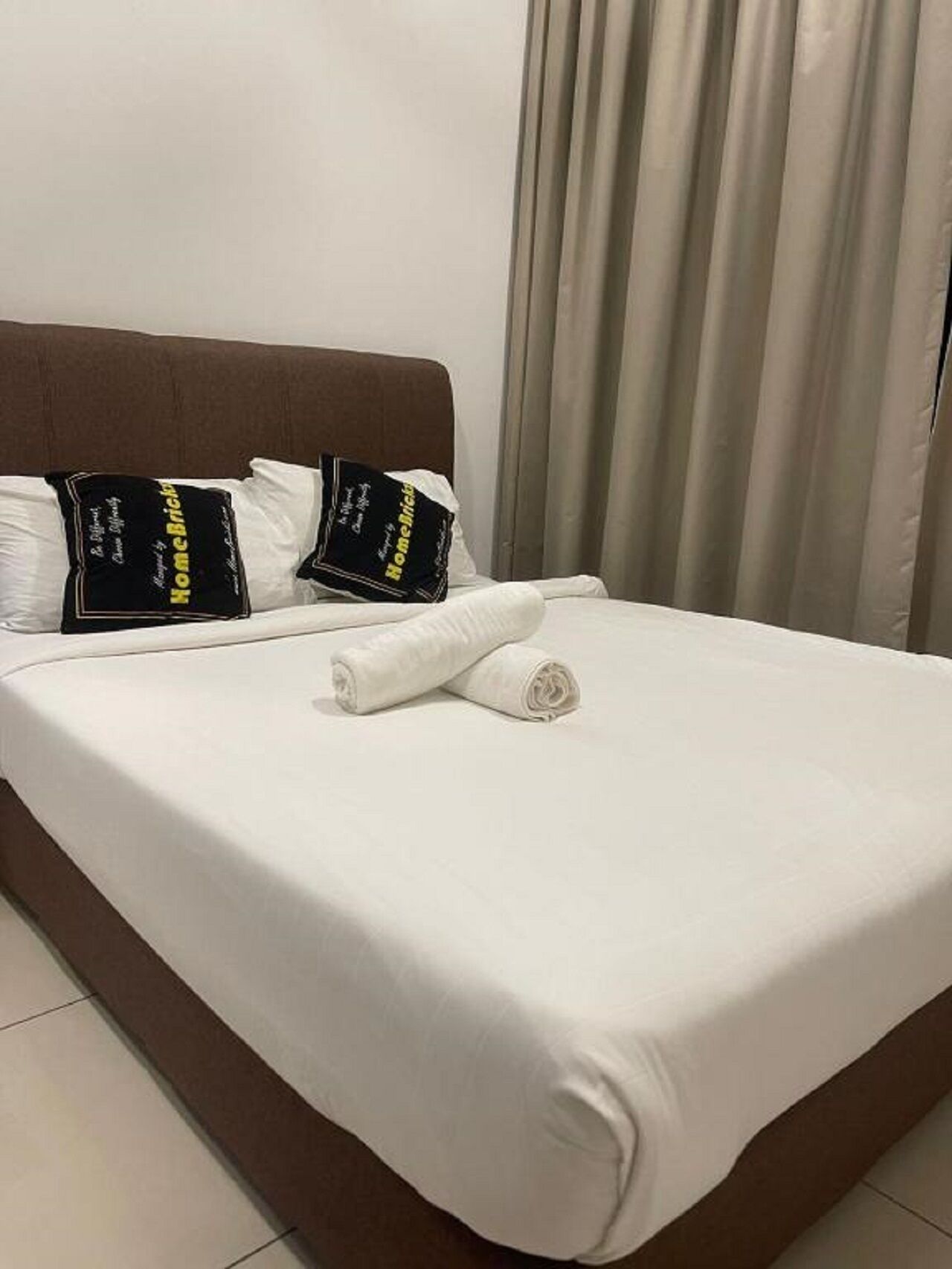 Ein ordentlich bezogenes Bett mit weißen Laken, zwei Kissen und einem aufgerollten Handtuch.