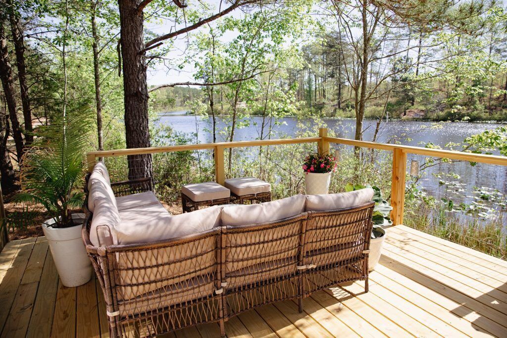 Ein Korbsessel mit Kissen auf einer Holzterrasse mit Blick auf einen See.
