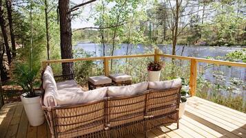Um sofá de vime com almofadas em um deck de madeira com vista para um lago.