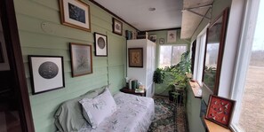 A room with a bed, framed pictures on the wall, a potted plant, and a window with a view.