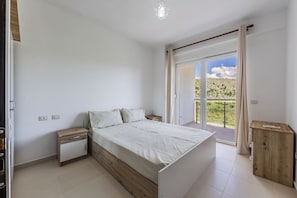 A bedroom with a bed, bedside tables, a wooden cabinet, and a sliding glass door leading to a balcony.