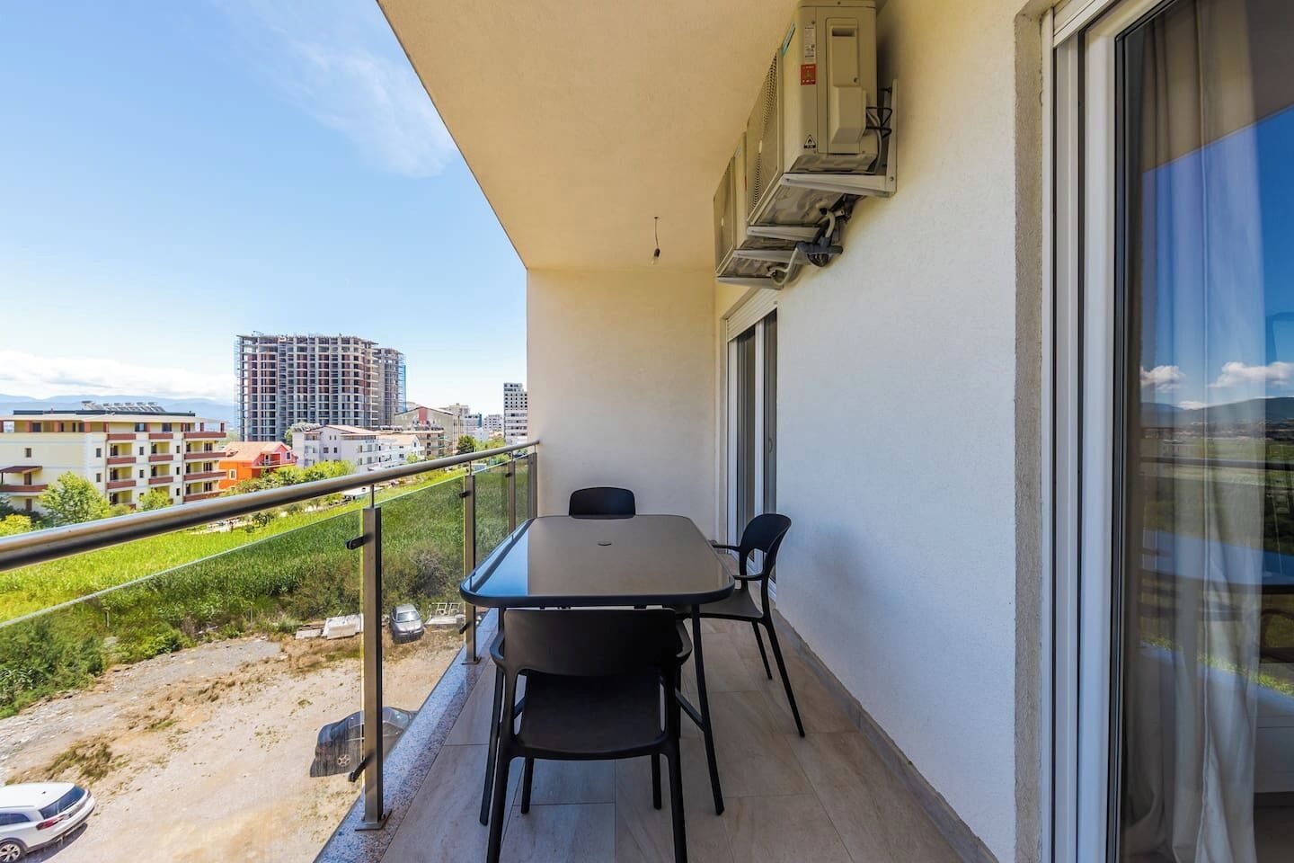A balcony with a table and chairs, a window, and an air conditioning unit.