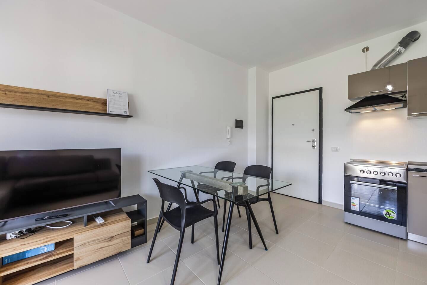 A modern apartment with a living room, a glass dining table with chairs, a kitchen with a stove, and a TV on a wooden stand.