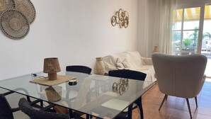 Un comedor con una mesa de vidrio, sillas de mimbre, un sofá blanco y detalles decorativos en la pared.