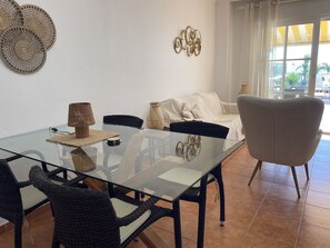 Ein Essbereich mit einem Glastisch, Korbstühlen, einem weißen Sofa und Wanddekoration.