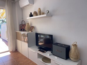 Ein modernes Wohnzimmer mit einem Flachbildfernseher, einem Marshall-Lautsprecher und dekorativen Gegenständen auf einem Regal.
