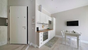 A modern kitchen with white cabinetry, a built-in oven, and a dining area with a table and chairs. - Hostdomus - Stella Maris (Alassio)