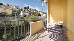 A balcony with a view of buildings, a table with cups and a bowl, and a railing. - Hostdomus - Stella Maris (Alassio)
