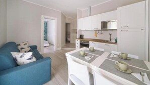 A modern kitchen with white cabinets, a stainless steel oven, and a dining area with a table set for two. - Hostdomus - Stella Maris (Alassio)