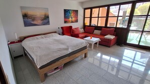A bedroom with a bed, a red sofa, a small table, and large windows. - Cozy vacation apartment with a beautiful terrace (Bad Windsheim)