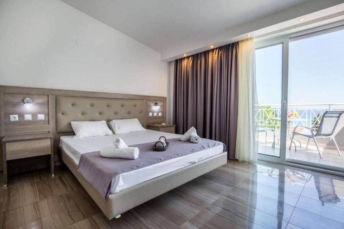 Habitación de hotel con una cama grande, una mesita de noche, una ventana con cortinas y un balcón con sillas.