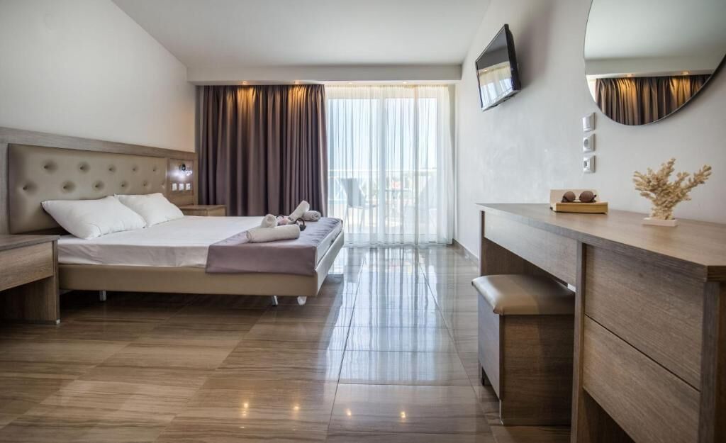 A modern hotel room with a large bed, a wooden dresser, a flat-screen TV, and a large window with curtains.