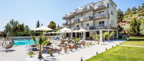 Un hotel de varios pisos con piscina, mobiliario exterior y un jardín ajardinado.
