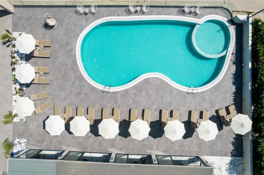 An aerial view of a swimming pool with a unique shape, surrounded by lounge chairs and umbrellas.