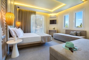 A modern hotel room with a bed, sofa, and ottoman, a small table, and a TV mounted on the wall. - Green Bay Thassos (Thasos)