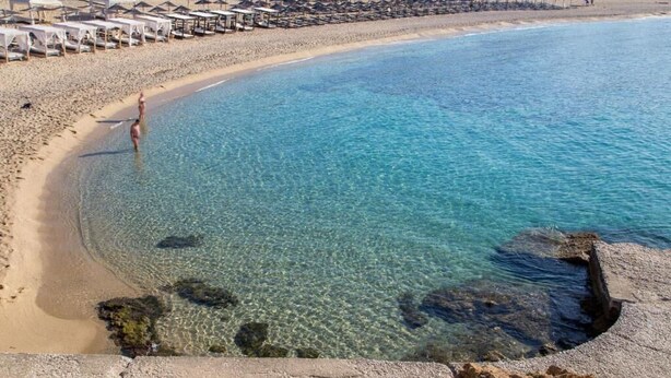 A beach with clear water, a rocky shoreline, and a row of beach umbrellas. - Green Bay Thassos (Thasos)
