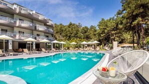 A swimming pool with lounge chairs and umbrellas, surrounded by a building with balconies. - Green Bay Thassos (Thasos)